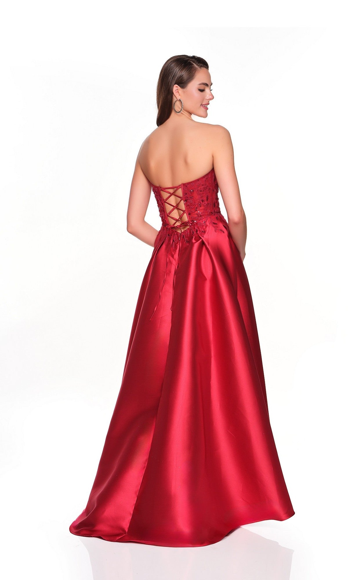 A woman stands against a white background wearing the Long Prom Dress: Dave and Johnny 12575, featuring a strapless corset bodice, lace-up back, and full satin skirt in bold red.